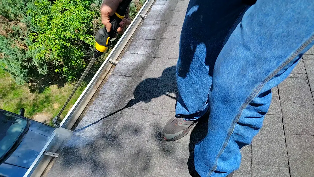 Applicator working a spray wand along the eave and gutter line of a shingle roof
