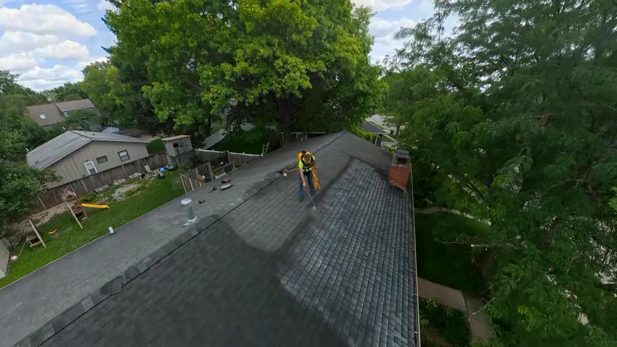 Wide aerial view of a treated asphalt shingle roof with the applicator at the ridge
