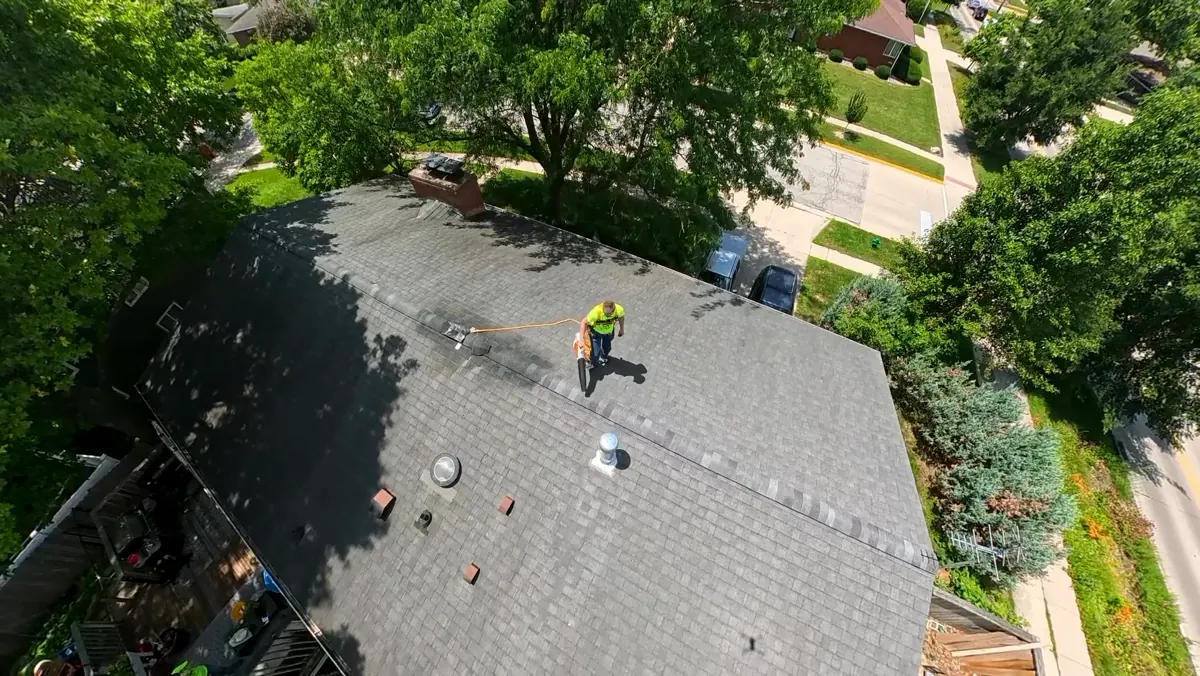 Applicator standing on an asphalt shingle roof, seen from above, looking over the slope
